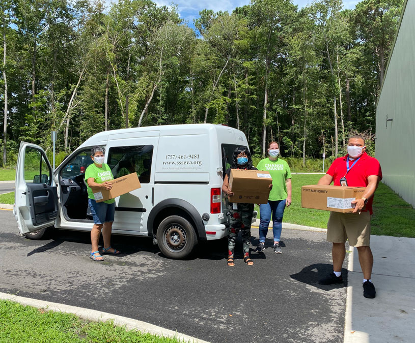 Four Senior Services staff and volunteers in green shirts loading boxed meals into a delivery van.