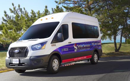 A white I-RIDE passenger van with the Senior Services logo parked on a tree-lined street.