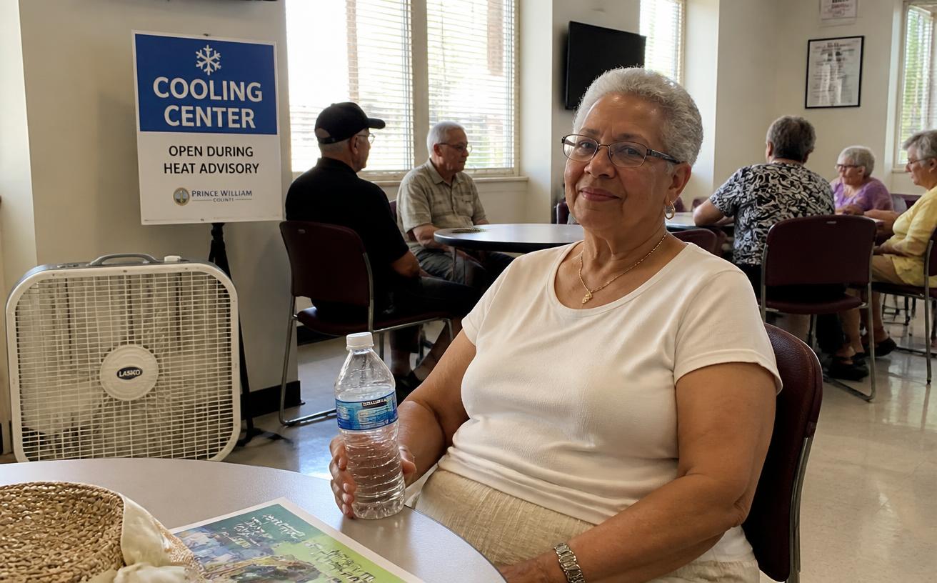 An older woman with a bottle of water resting inside an open cooling centre.